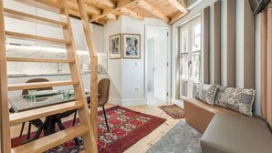Ein Zimmer mit Hochlitzer, einer Holzleiter, einer Couch mit gemusterten Kissen, einem rot-weißen Teppich und einer Tür zu einem anderen Raum.