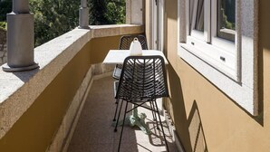 Ein Balkon mit Tisch und Stühlen, ein Fenster und Blick auf Bäume.