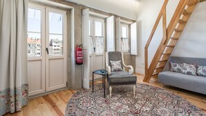 A room with a wooden staircase, a grey sofa, a patterned rug, and a chair.
