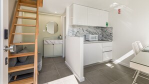 A compact kitchen with white cabinets, a marble countertop, a microwave, and a wooden ladder.