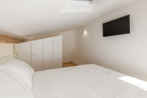 Une chambre à coucher comprenant un lit, une armoire, un téléviseur et une fenêtre de toit.