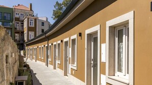 A row of hotel rooms with individual doorways and windows, a stone wall on one side, and a clear sky. - Homey Studio by PortoDreamStays (Porto)