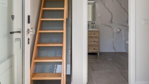 A modern interior with a wooden staircase, a marble wall, and a bathroom with a vanity. - Homey Studio by PortoDreamStays (Porto)