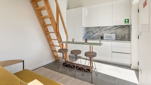 A modern kitchen with white cabinets, a marble backsplash, a glass table with stools, and a wooden ladder. - Spacious Bright Studio by PortoDreamStays (Porto)