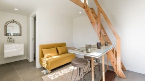 A modern loft bedroom with a sloped ceiling, a sofa, a glass dining table, and a wooden staircase. - Spacious Bright Studio by PortoDreamStays (Porto)