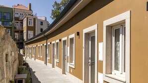 A row of hotel rooms with individual doorways and windows, a paved walkway, and a stone wall on one side. - Airy Studio by PortoDreamStays (Porto)