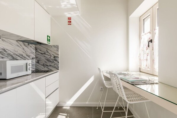 A modern kitchen with a microwave, white cabinets, a glass table, and a window with floral curtains.