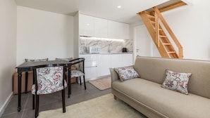 Ein kompakter Wohnbereich mit Essplatz, Sofa, Küche und einer Holztreppe.
