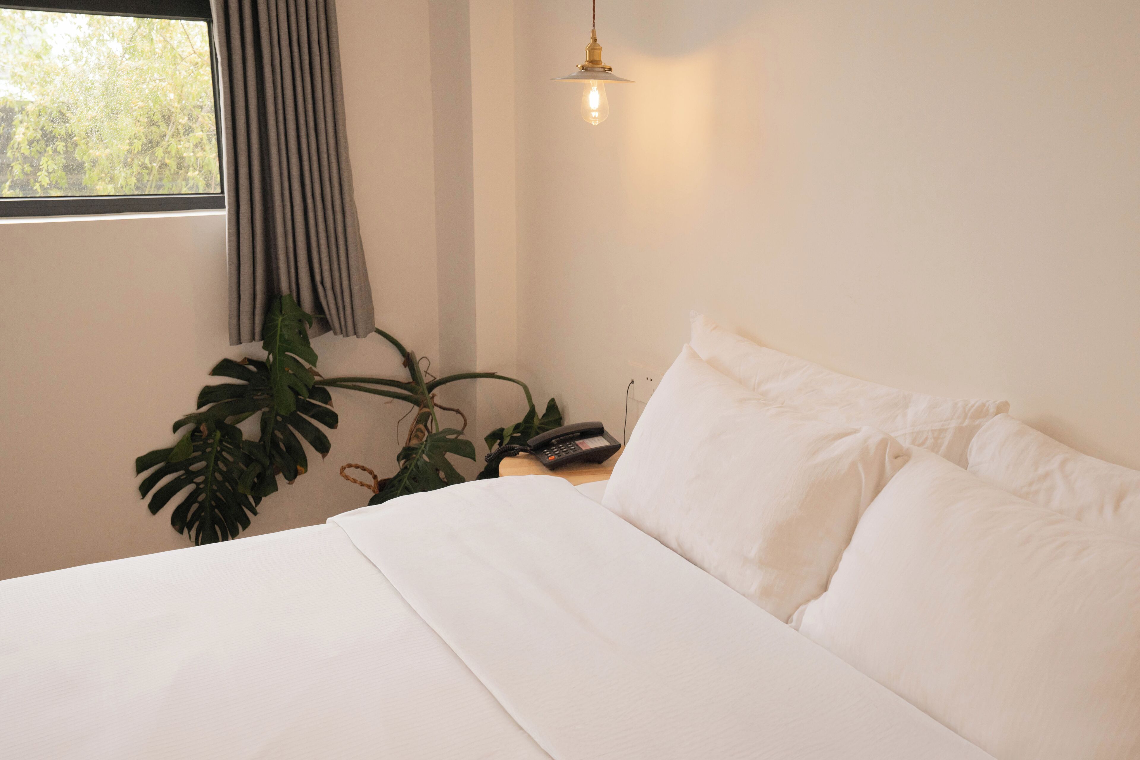 A neatly made bed with white linens, a bedside telephone, and a hanging light fixture.