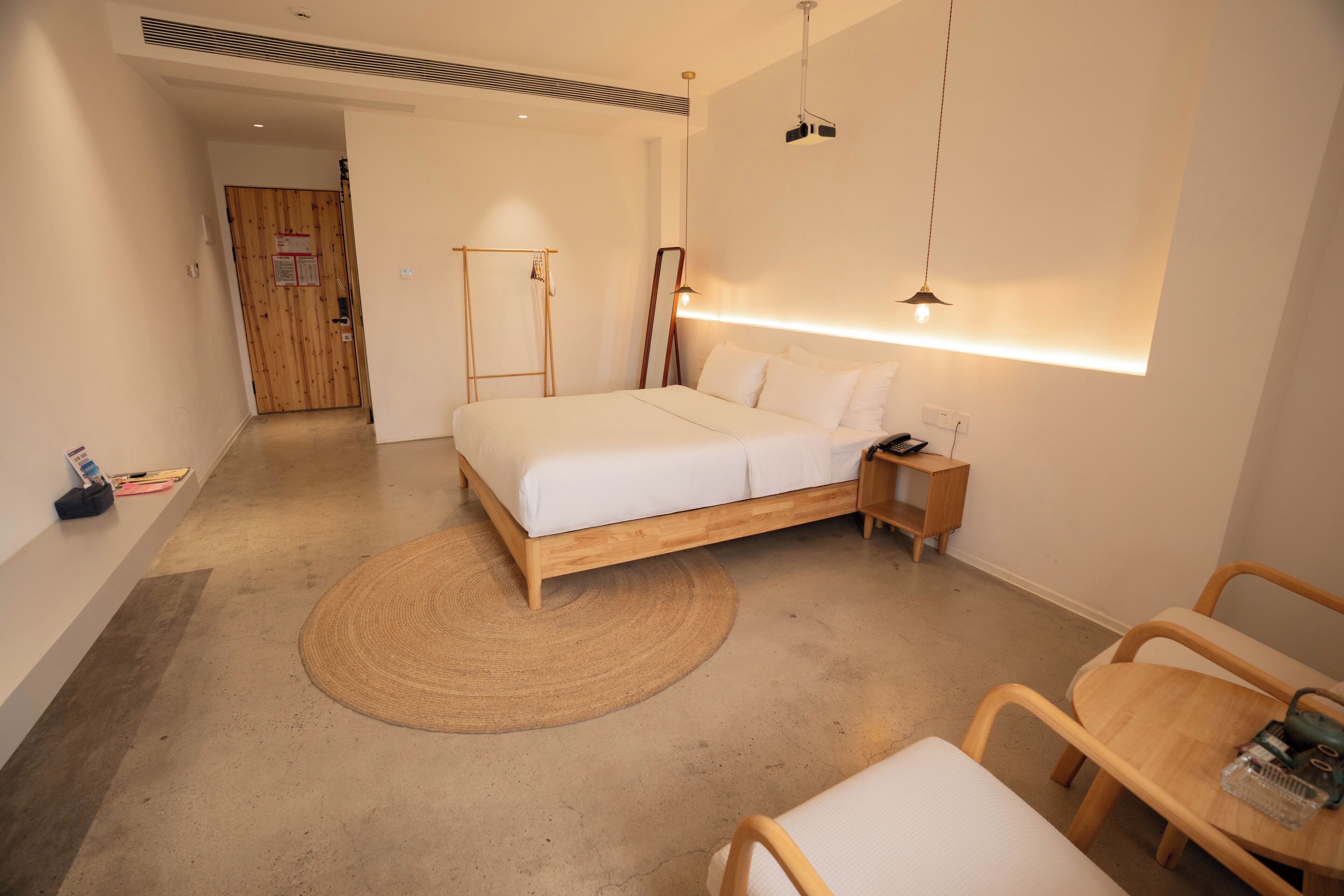 A modern hotel room with a wooden bed, bedside table, and a small wooden chair.