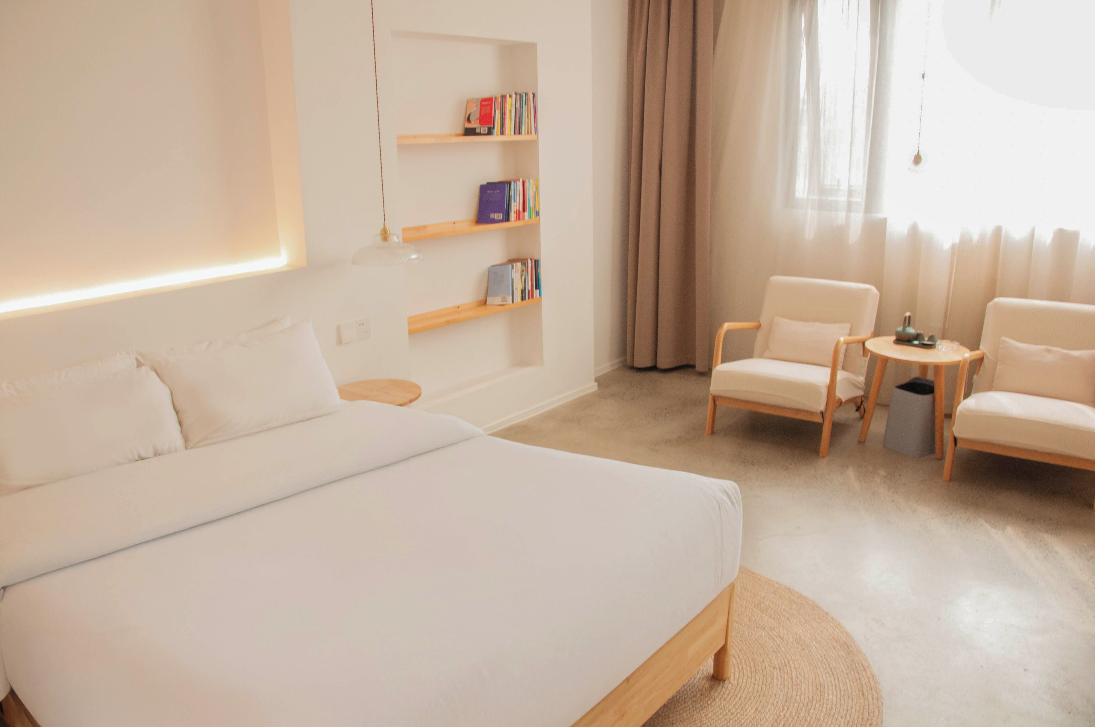 Ein modernes Hotelzimmer mit einem großen Bett, zwei Sesseln, einem kleinen Tisch und einem Bücherregal.