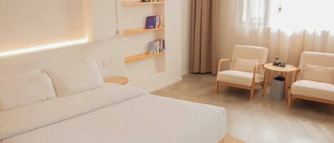 Ein modernes Hotelzimmer mit einem großen Bett, zwei Sesseln, einem kleinen Tisch und einem Bücherregal.