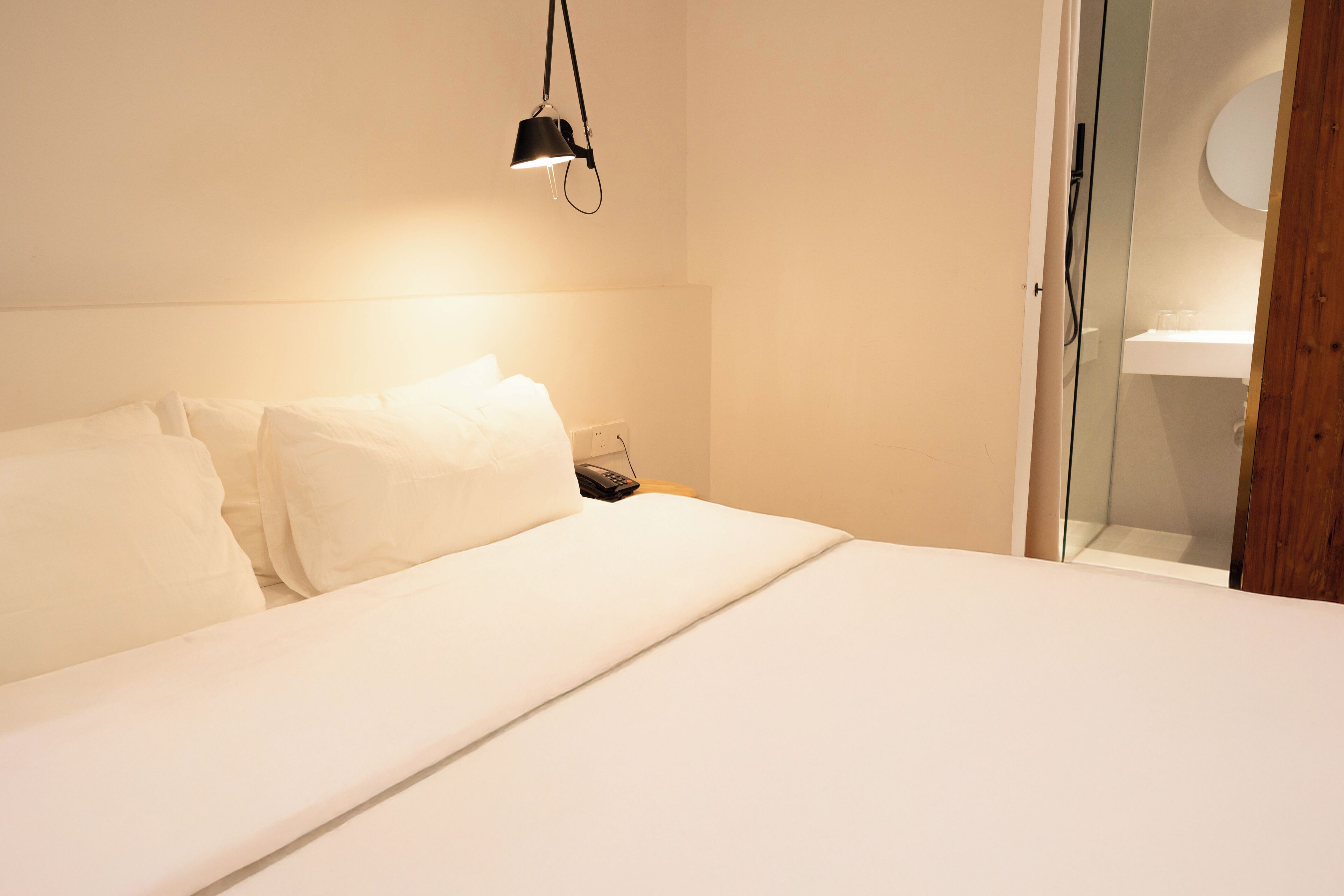 Una camera d'albergo con un letto, un comodino, una lampada e una porta in vetro che dà su un bagno.