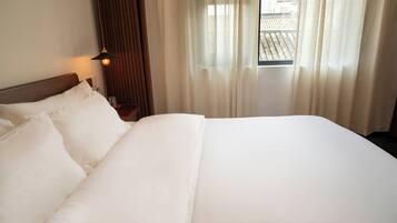 Una habitación de hotel con una cama grande, una mesita de noche, una lámpara y una ventana con cortinas.