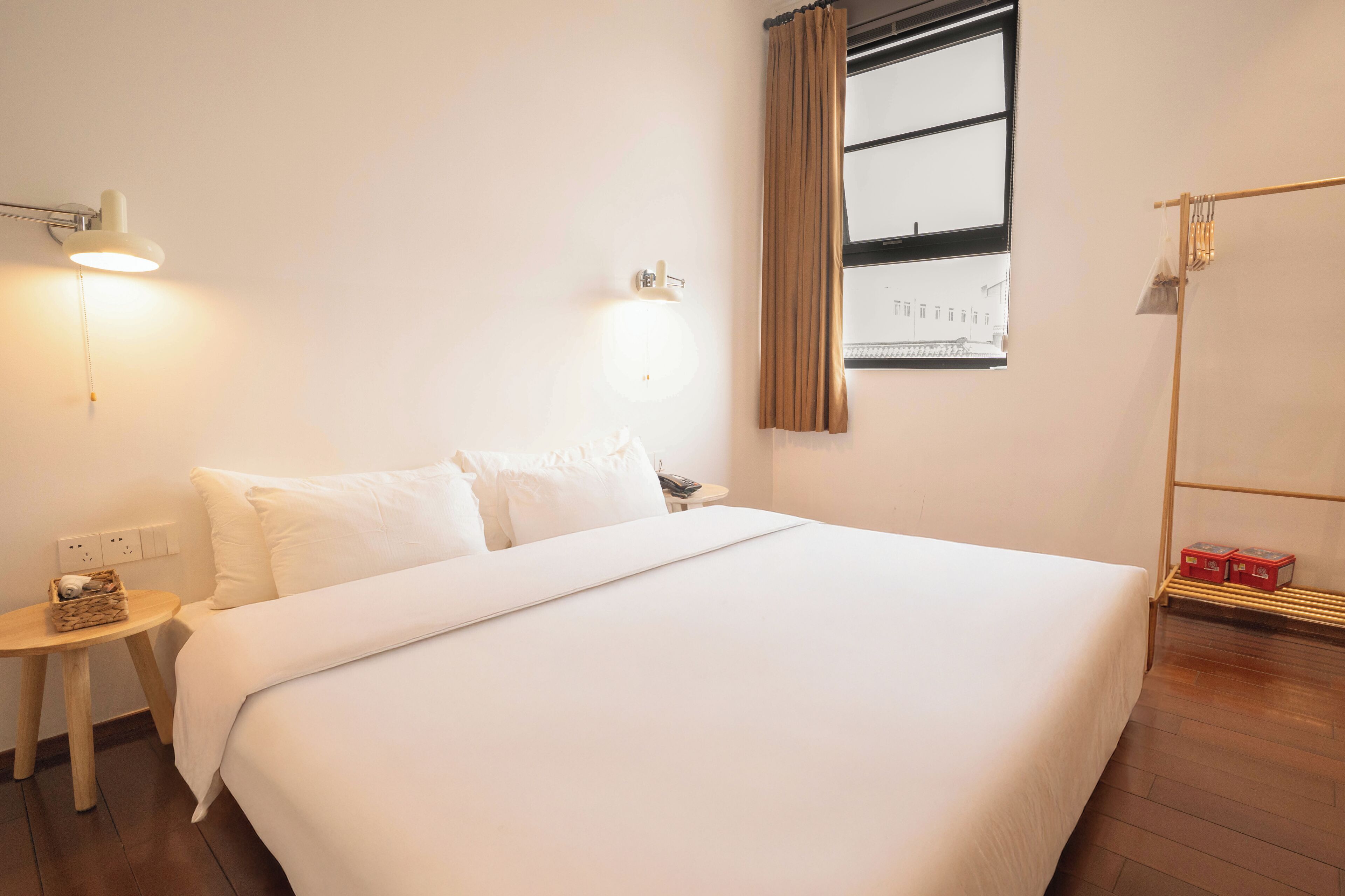 A neatly made bed with white linens, a bedside table with a lamp, and a window with curtains.