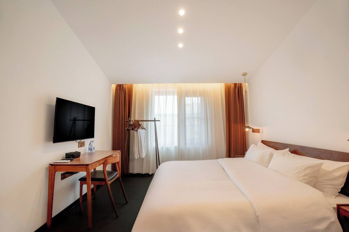 A hotel room with a bed, a desk, a chair, a television, and a window with curtains.