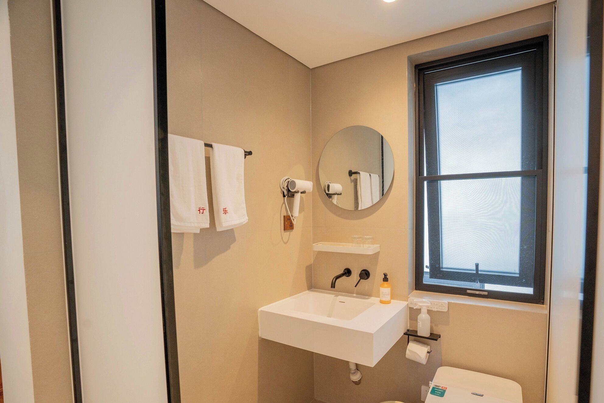 Een badkamer met een wastafel, spiegel, handdoekhouder, raam en toilet.