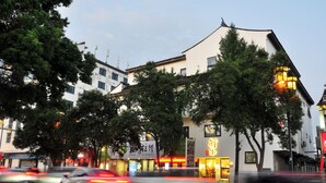 A building with a traditional architectural style, a storefront with illuminated signage, and a street with moving vehicles. - Xingle Hotel (Suzhou)