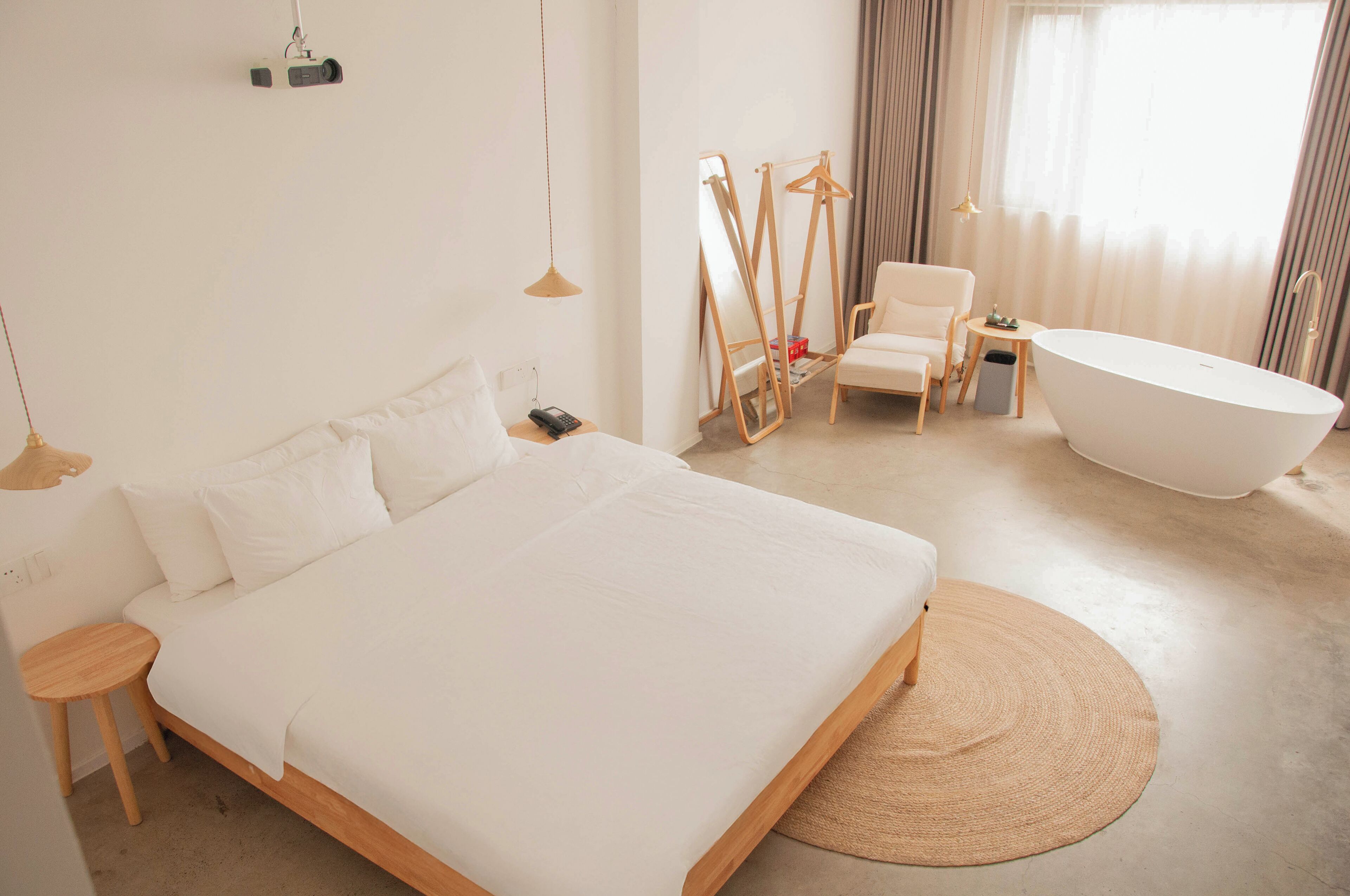 A modern bedroom with a large bed, a chair, a bathtub, and a mirror.