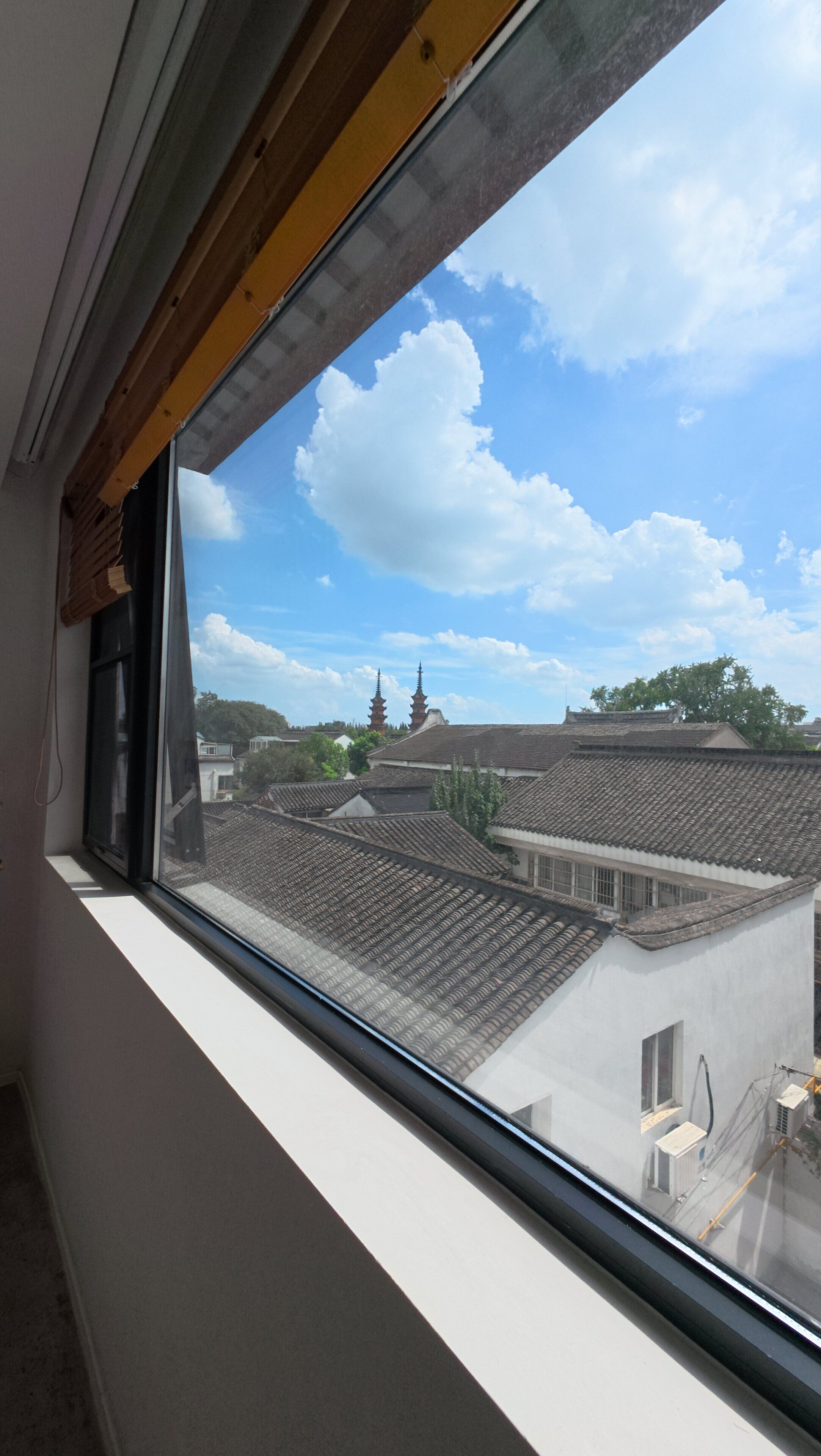 Une fenêtre donnant sur des bâtiments traditionnels et un ciel dégagé.