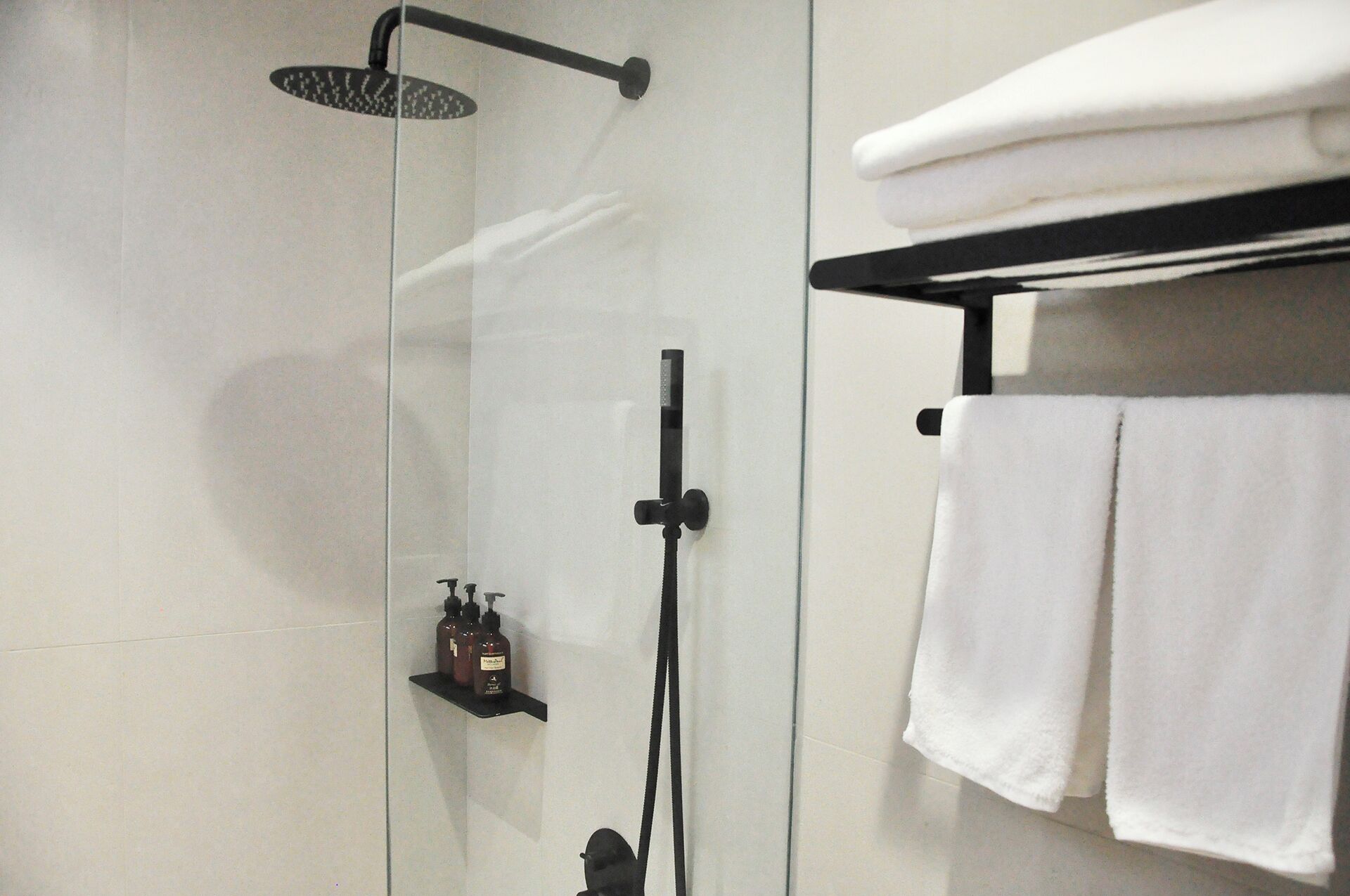 Un baño moderno con cabina de ducha de vidrio, un toallero negro con toallas dobladas y un estante con artículos de aseo.