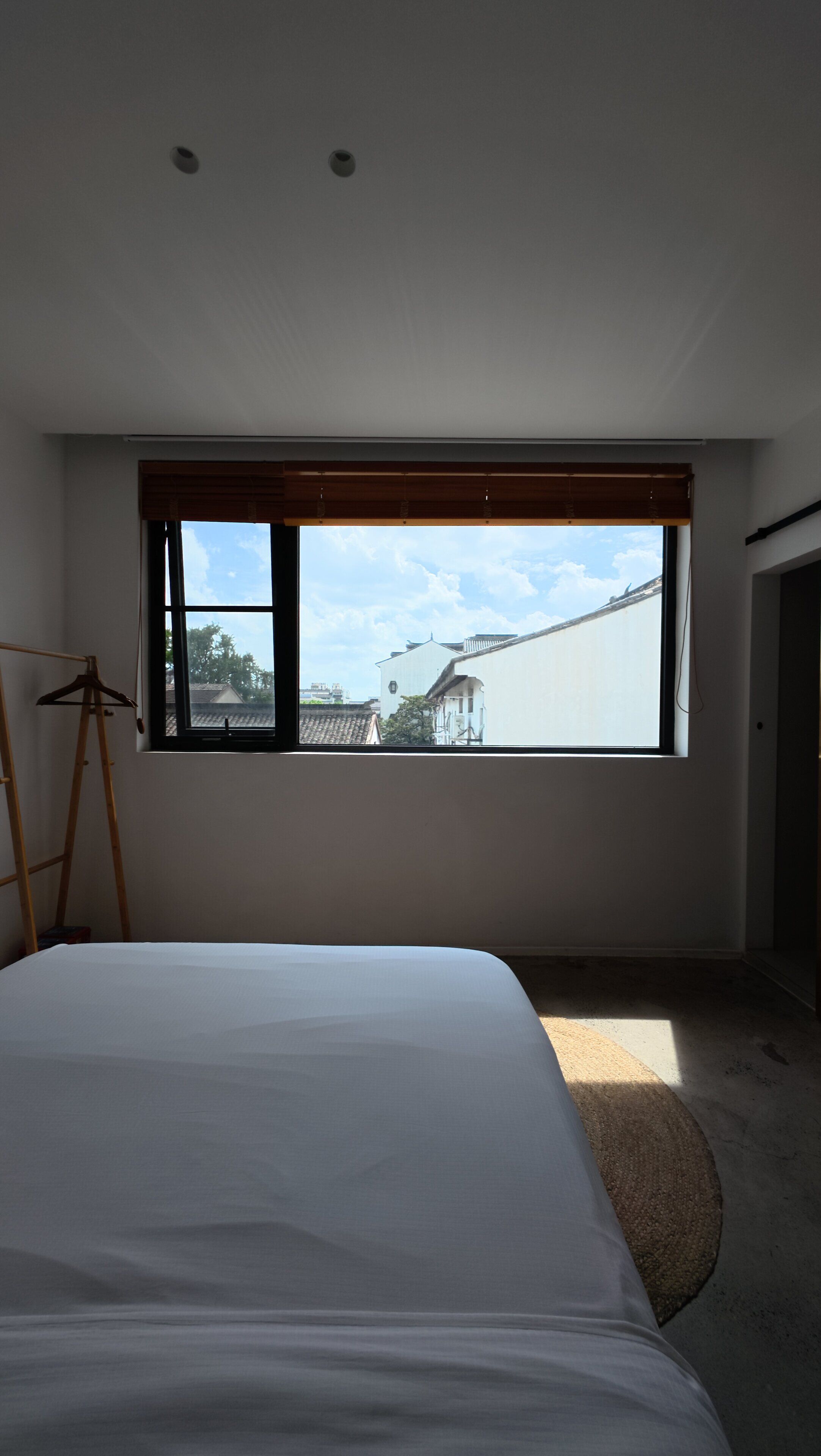 Ein Schlafzimmer mit großem Fenster, einem Bett, einem Holzgalgen und einer Leiter.