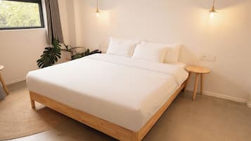 A bedroom with a large bed, two bedside tables, a small round table, and a potted plant.