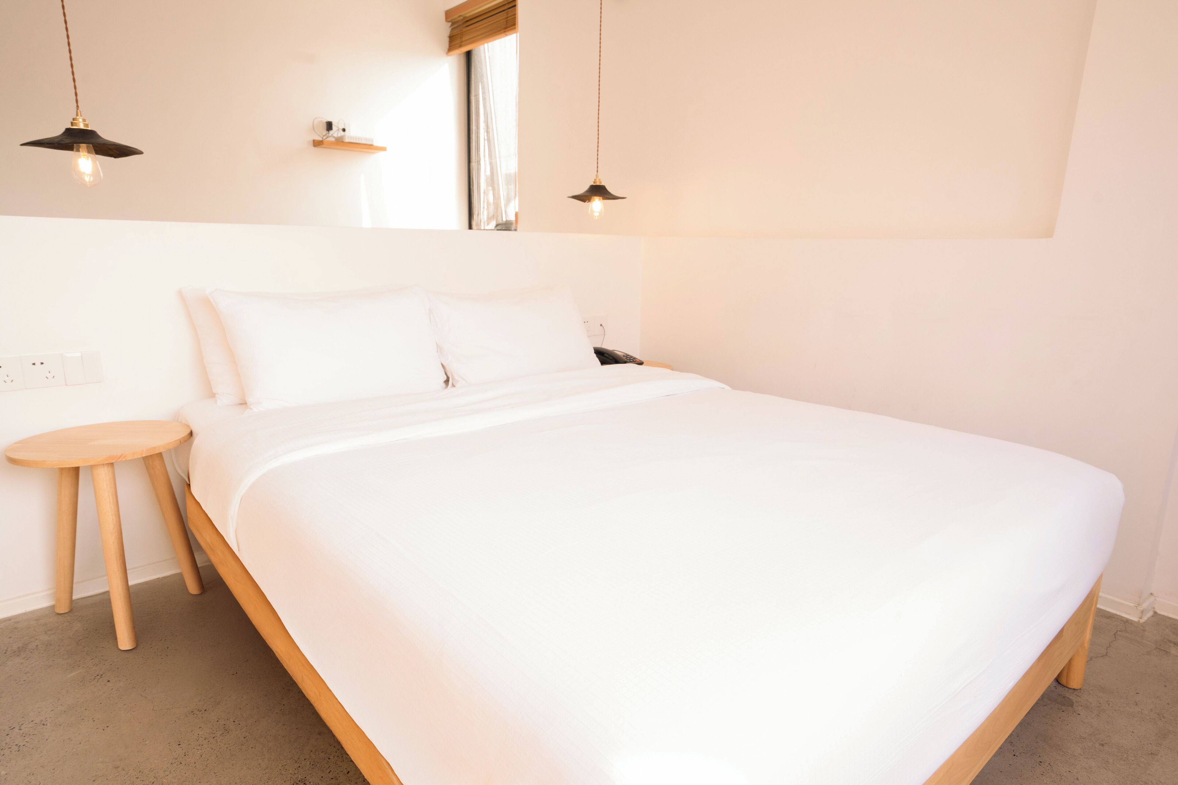 A bedroom with a large bed, wooden headboard, two bedside tables, and pendant lights.