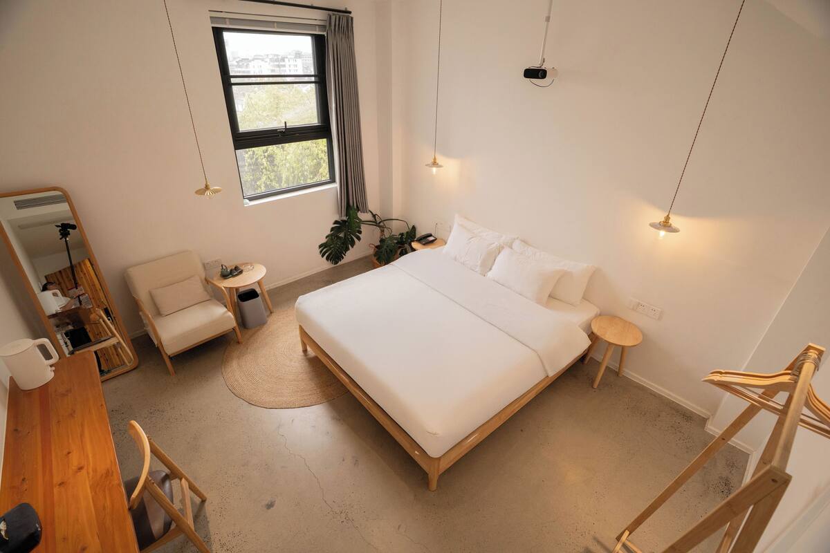 A bedroom with a large bed, a desk, a chair, a small table, and a mirror.