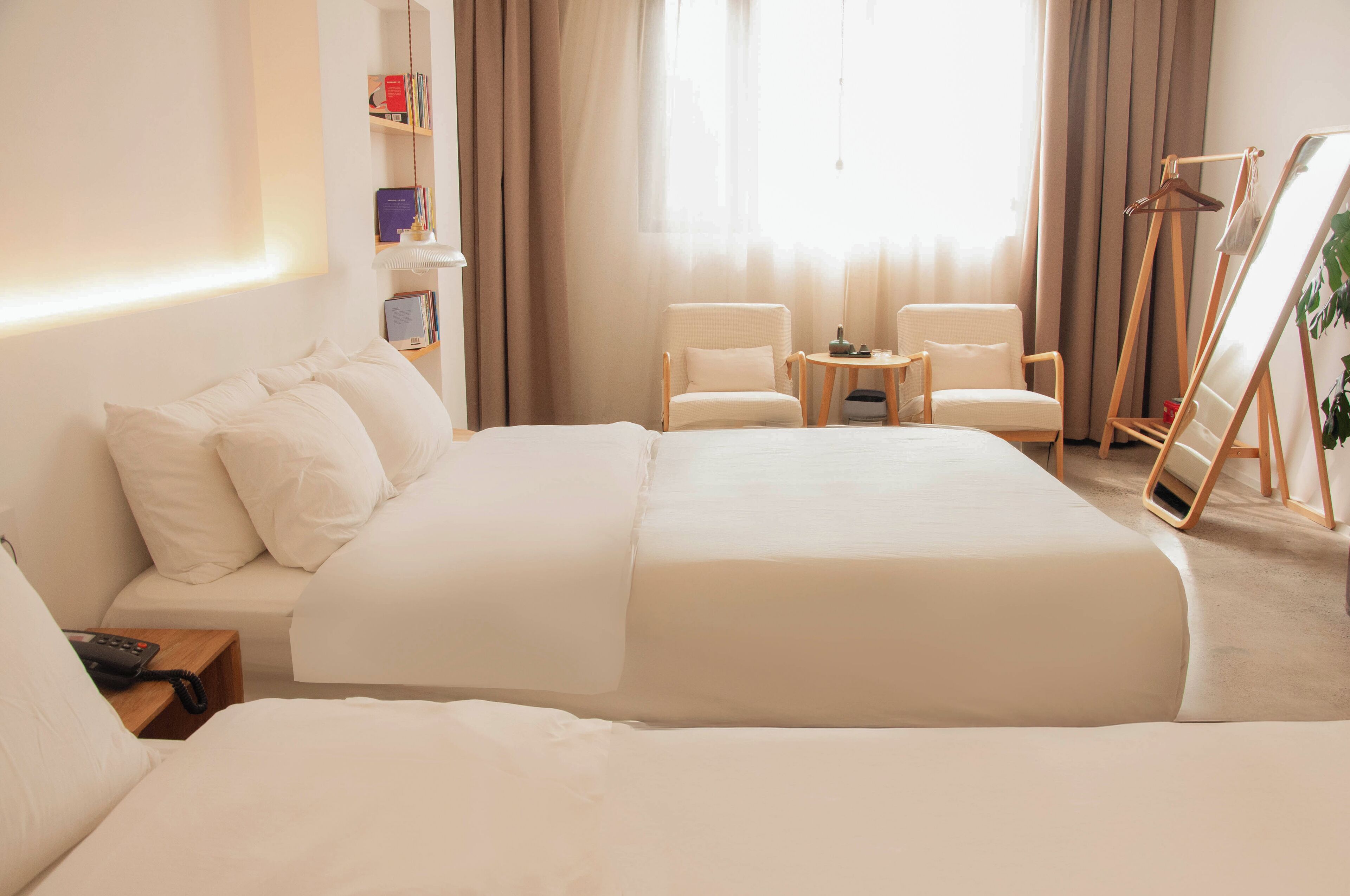 Ein Hotelzimmer mit einem großen Bett, einem Nachttisch mit Telefon, einem kleinen Tisch mit Stühlen, einem Bücherregal und einem Gemälde an der Wand.