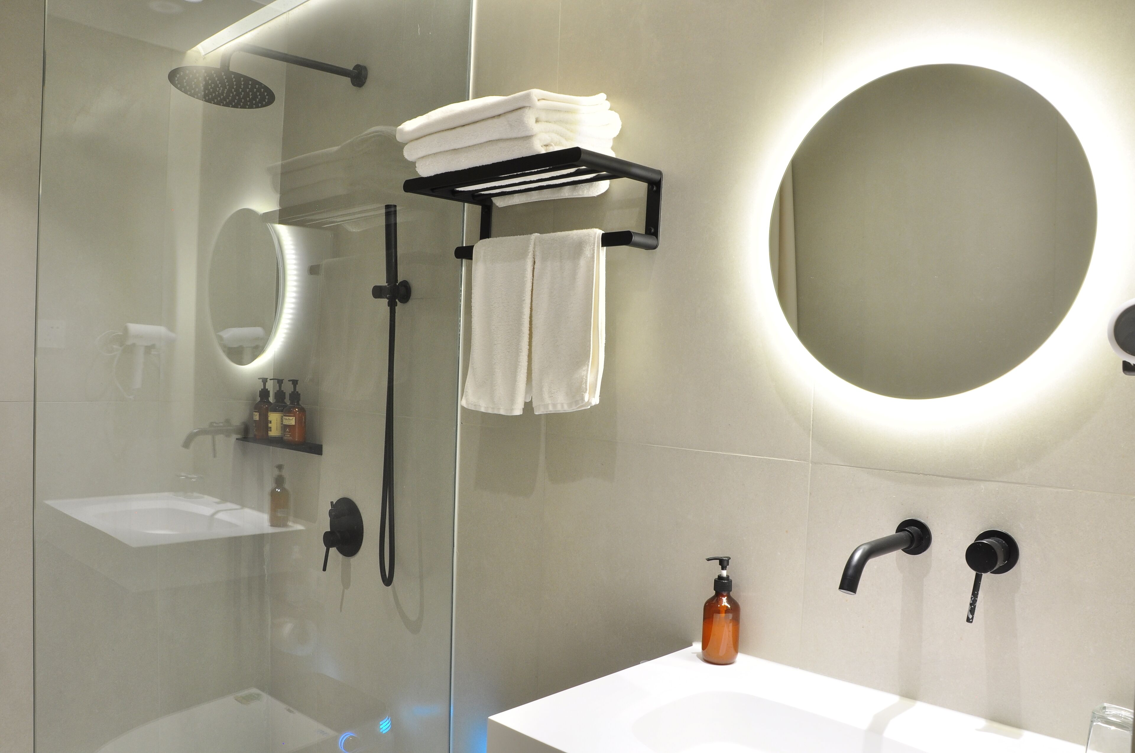 A modern bathroom with a glass-enclosed shower, a white sink, and a round mirror.