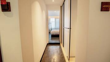 Un estrecho pasillo con suelo de madera que conduce a un dormitorio con cama y ventana.