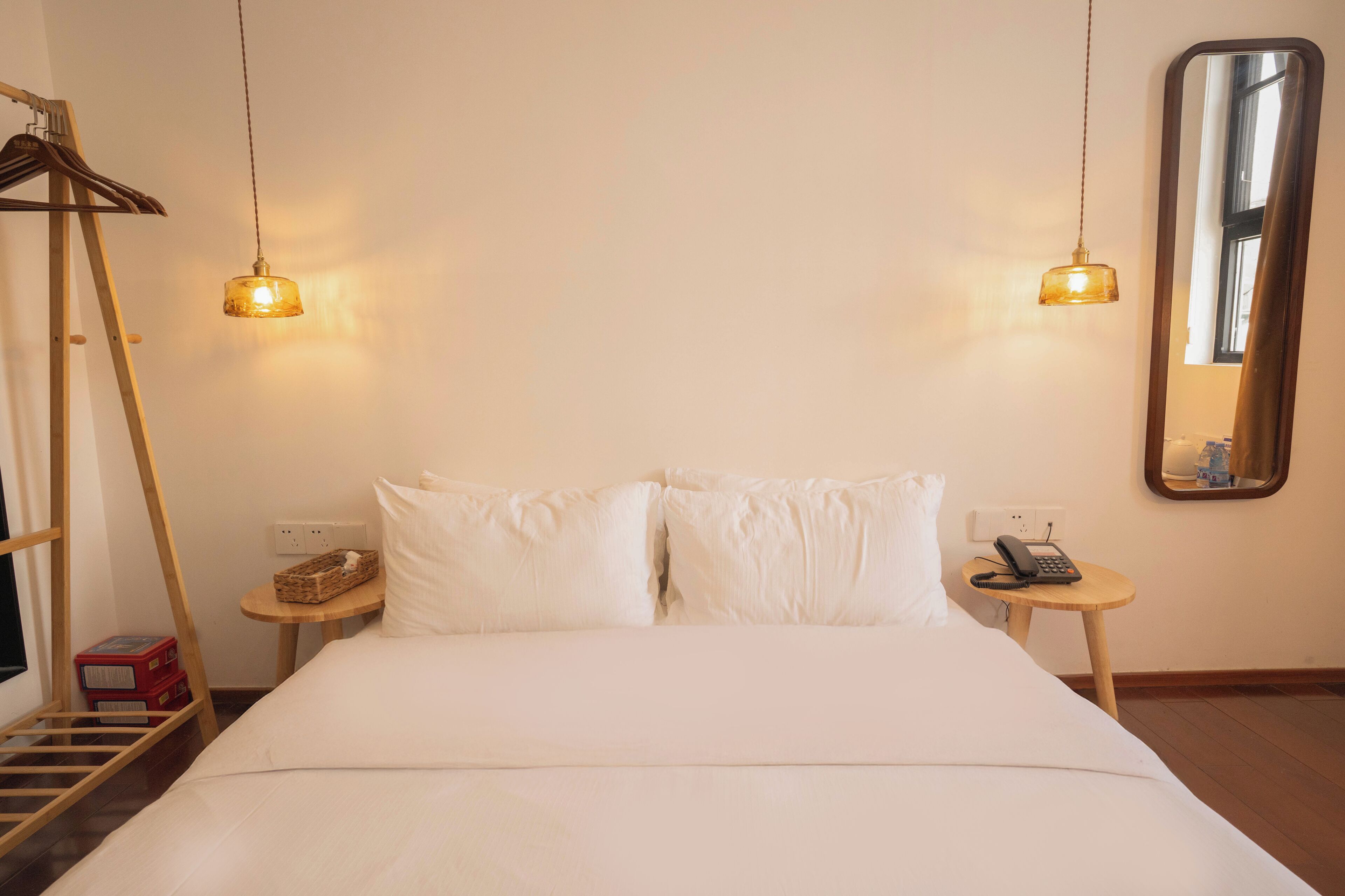 A hotel room with a bed, two bedside tables, a mirror, and a hanging light fixture.