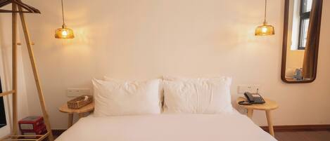 A hotel room with a bed, two bedside tables, a mirror, and a hanging light fixture.