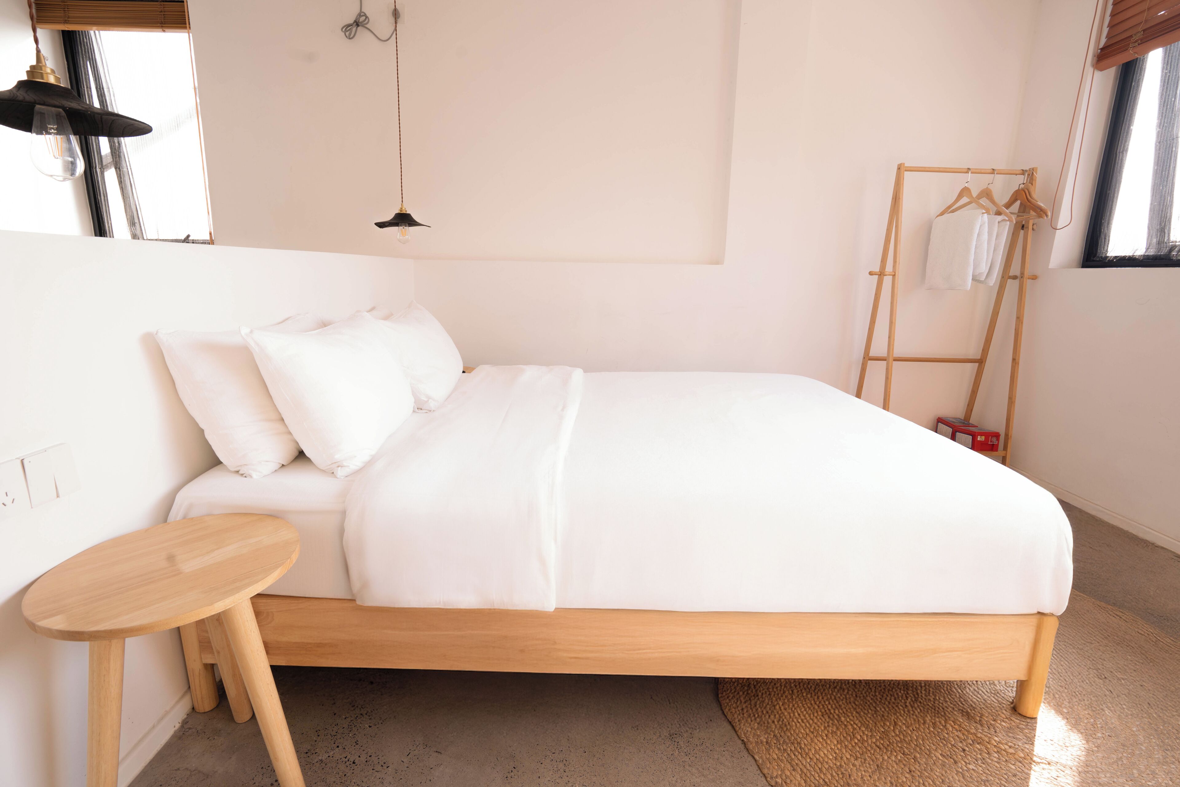 A minimalist bedroom with a wooden bed, a small wooden side table, and a wooden clothes rack with hangers.