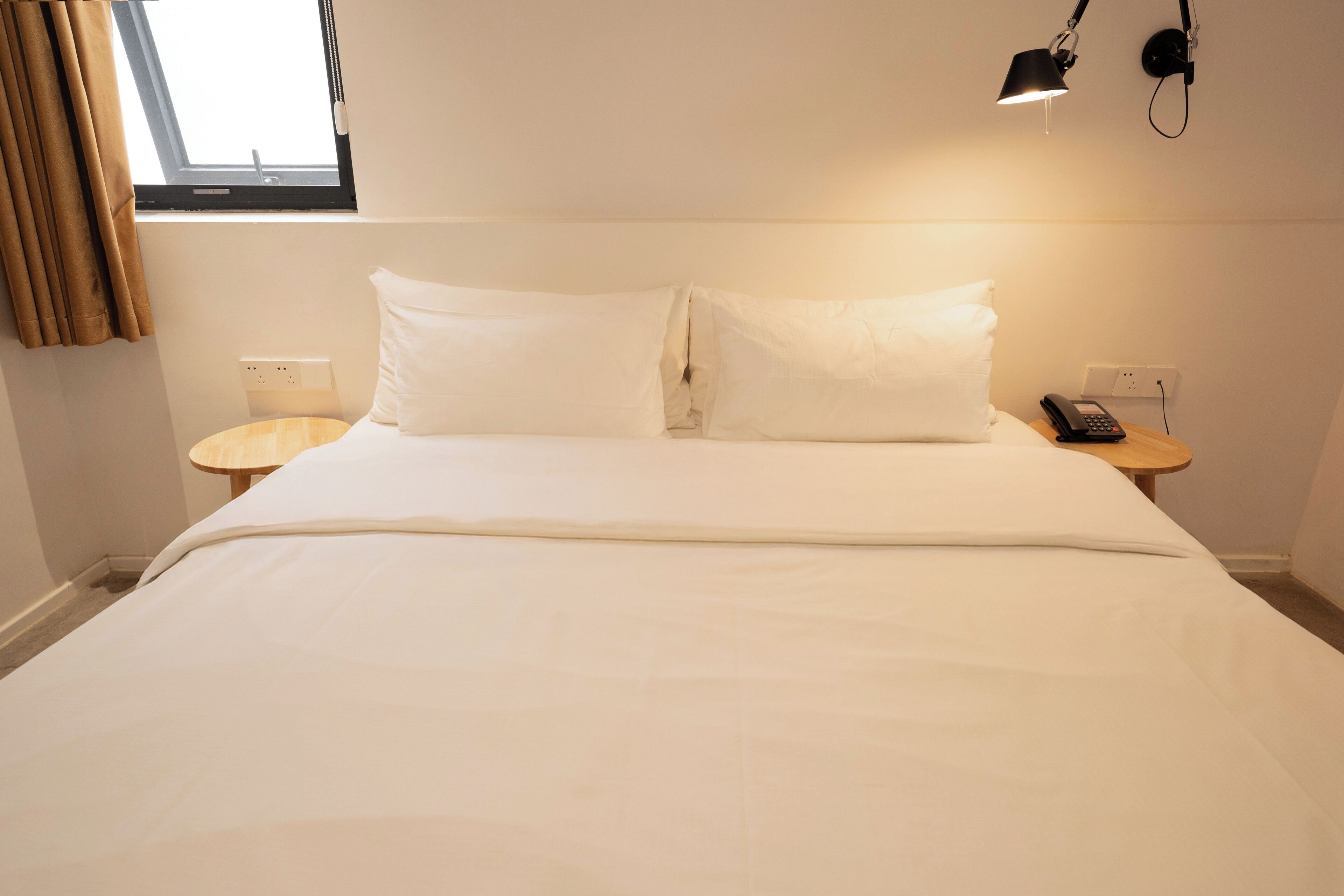 A neatly made bed with white linens, a bedside table with a lamp, and a phone on the right side.