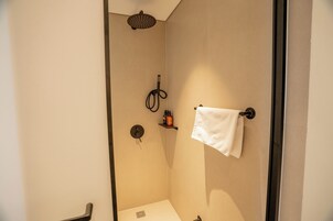 Un baño con ducha, un perchero y un estante con artículos de aseo.