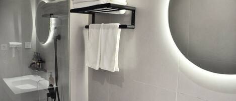 A modern bathroom with a glass-enclosed shower, a towel rack with folded towels, and a large sink.