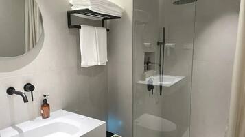 Un baño moderno con ducha de vidrio, lavamanos blanco y retrete.