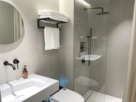 Un baño moderno con ducha de vidrio, lavamanos blanco y retrete.