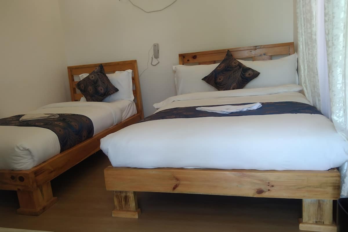 Two wooden beds with white linens and patterned pillows, a bedside telephone, and a window with curtains.