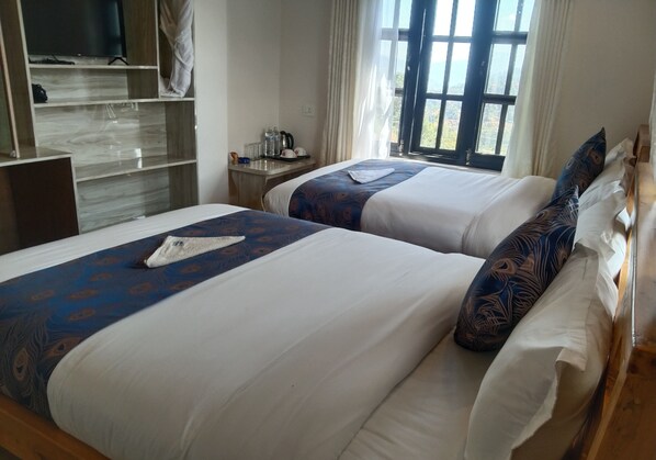 Two beds with white and blue bedding, a wooden desk, a television, and a window with curtains. - Thumki Resort (Panaoti)