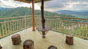 Un balcón techado con una mesa rústica y taburetes, con vistas a un paisaje montañoso.