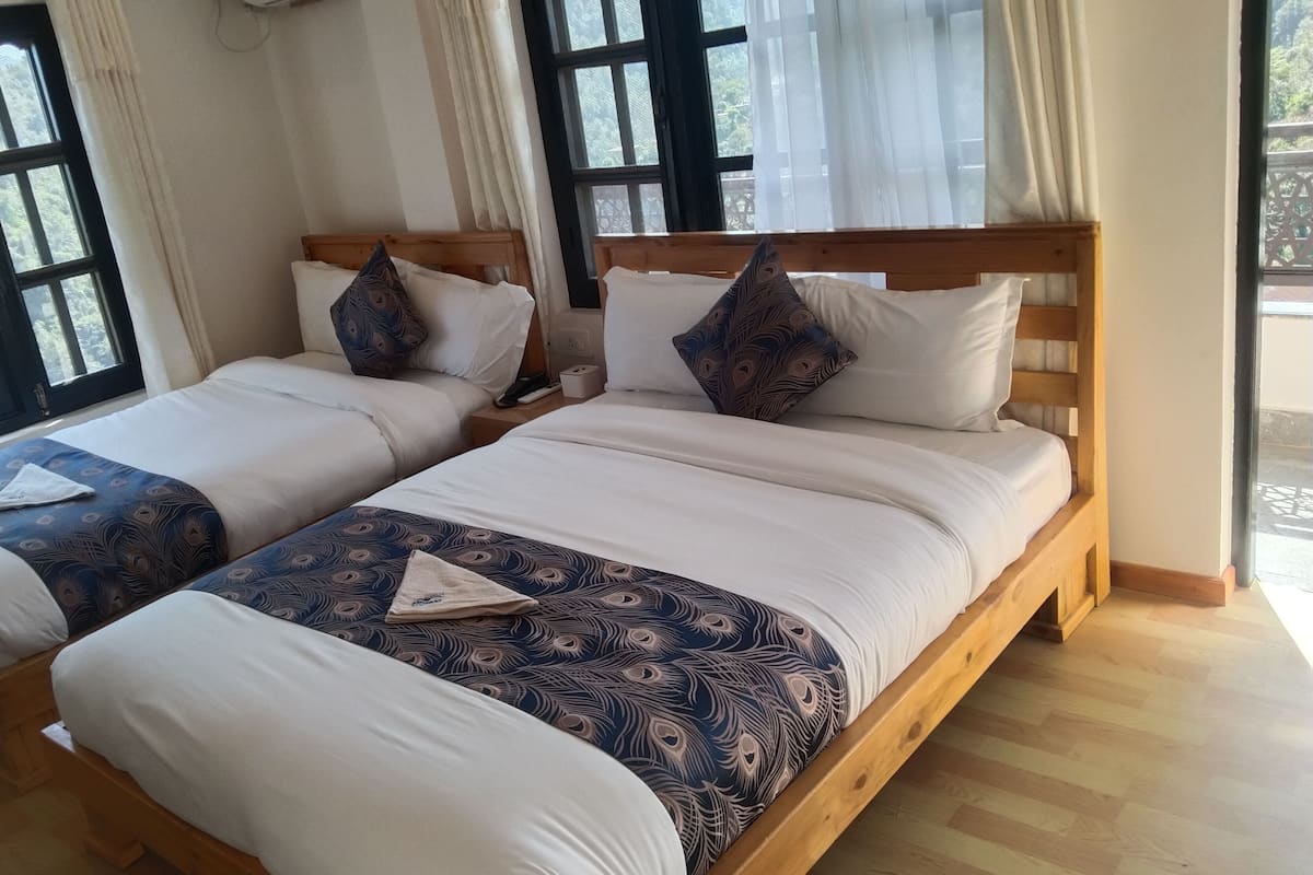 A hotel room with two wooden beds, white bedding, and a peacock-patterned bedspread.