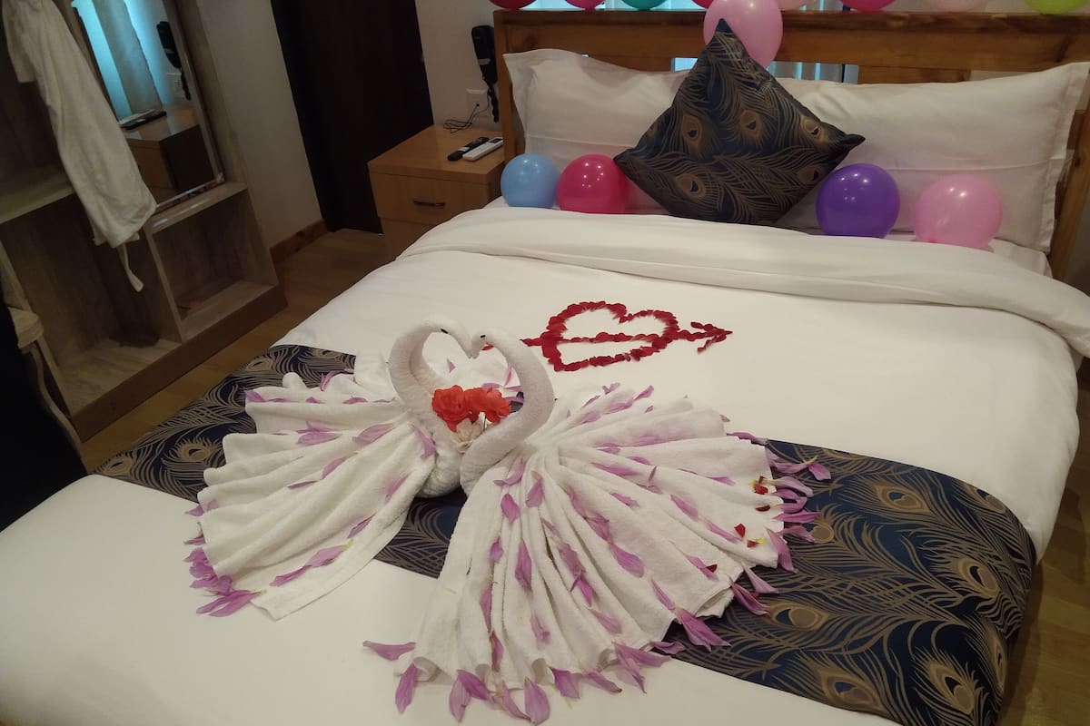 A neatly made bed with a towel swan centerpiece, a heart design, and balloons.