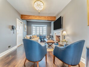 Een woonkamer met een open haard, een groot raam, een flatscreen televisie en blauwe stoelen.