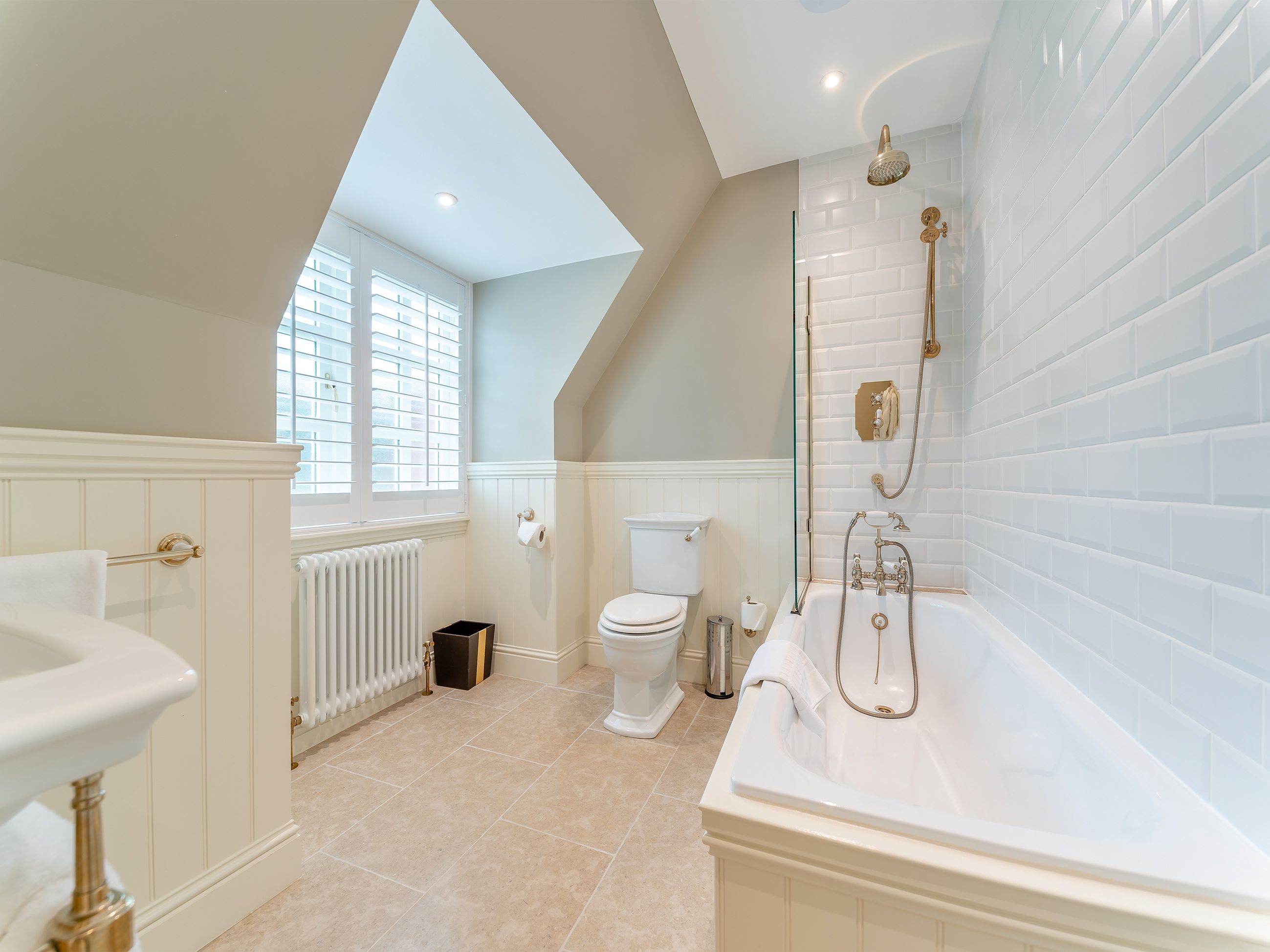 A bathroom with a bathtub, toilet, and sink, featuring a sloped ceiling and a window.