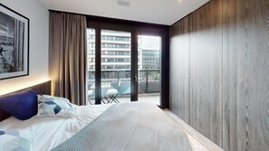 Een moderne slaapkamer met een groot bed, uitzicht op de stad door middel van van top tot teen raam en een balkon met buitenmeubilair.