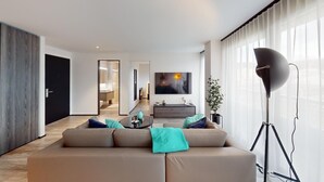 A modern living room with a sofa, a coffee table, and a floor lamp. There is a TV mounted on the wall and a door leading to another room.