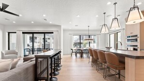A modern kitchen with a bar area, large windows, and a dining space. - Modern Oasis at Desert Color (by Ember Stays) (St. George)